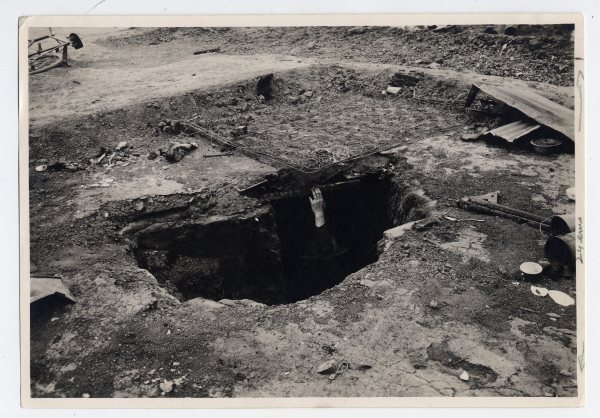 Man examines pit beneath where a tent had stood on its platform. (1914)